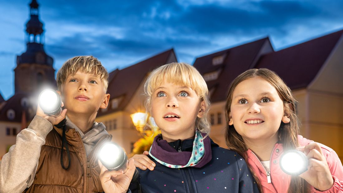 Drei Kinder stehen bei Dunkelheit auf dem Marktplatz in Luth. Eisleben und schauen neugierig nach vorn mit ihren Taschenlampen in der Hand Drei Kinder stehen bei Dunkelheit auf dem Marktplatz in Luth. Eisleben und schauen neugierig nach vorn mit ihren Taschenlampen in der Hand